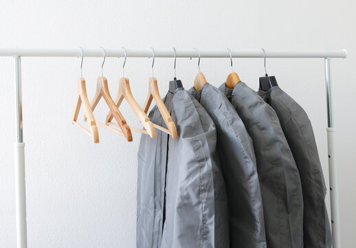 Garment storage bags protect seasonal clothes on rack with wooden hangers. Fabric care dry cleaning dust protection closet organization. Seasonal wardrobe change smart housekeeping.