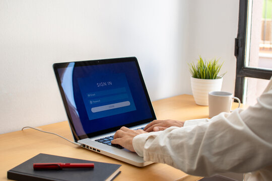 Man typing on laptop keyboard at wooden desk to log in to online account in home office