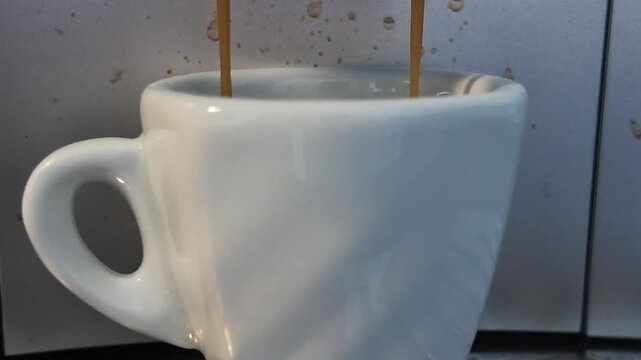 Coffee brewing in a white cup in a kitchen, with coffee spilling over the edge