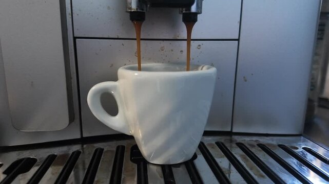 Making coffee in a machine with an espresso shot pouring into a white cup in a kitchen