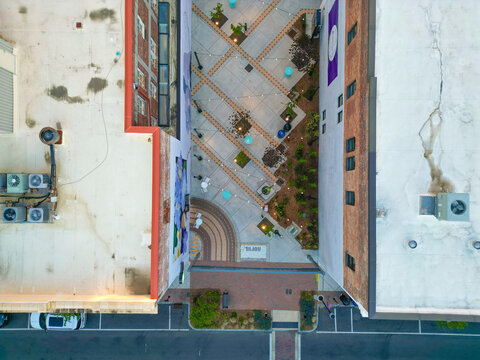 Aerial view of a pedestrian alleyway with string lights, landscaping, and patterned pavement between historic brick buildings in downtown Wilmington, North Carolina, United States.