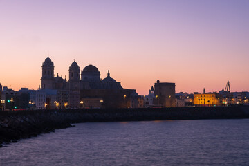Silhouettes of Cadiz Cathedral and old town buildings along the ocean promenade against a colorful dawn sky in Cadiz, Andalusia, Spain. © nzatravel