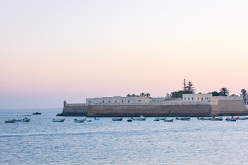 Santa Catalina Castle before sunrise surrounded by ocean waters filled with small fishing boats in Cadiz, Andalusia, Spain. © nzatravel
