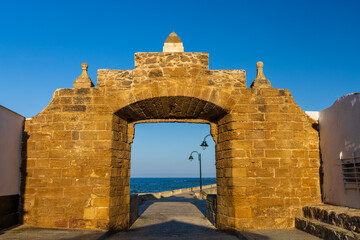Naklejka premium Historic stone wall of Puerta de la Caleta with an archway leading to the causeway toward San Sebastian Castle in Cadiz, Andalusia, Spain.