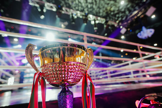 Golden trophy with colorful ribbons displayed in a boxing ring under dramatic arena lights, symbolizing victory, achievement and sporting success.
