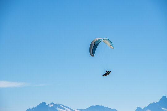 Aerial view of a paraglider soaring through the clear blue sky above the snow-capped peaks of the Bernese Alps near Stockhorn, Erlenbach im Simmental, Canton of Bern, Switzerland.