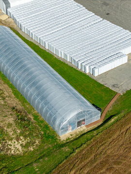 Aerial view of compressed peat bales wrapped in white plastic stacked neatly next to a large greenhouse at a processing facility in Krimulda Parish, Sigulda Municipality, Latvia.