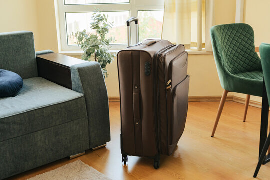 Closed brown luggage standing on a wooden floor in a modern living room ready for travel.
