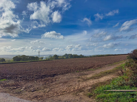 Ploughed Farm Field in Rural Devon Landscape with Telegraphed Pole and Cloud Sky