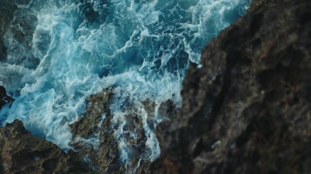 Sea Waves Crash Against Rugged Rocks Along Balis Coast, Swirling Into Frothy White Water. Turquoise Surf Surges Through Narrow Gaps, Creating Dramatic View Of Nusa Dua Shoreline.