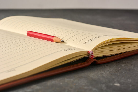 red pencil on open lined notebook on dark desk, blank yellow paper and brown leather cover book in soft focus with copy space, creative writing and education background