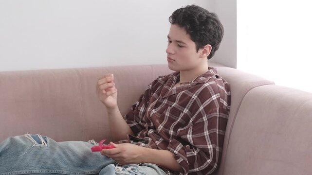 Worried teenager biting nails on sofa, teen boy with red game controller thinking and looking down. Anxiety and gaming stress concept, upset young man