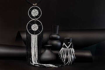 African beaded statement earrings featuring bold geometric patterns and cascading black and white strands, styled with sculptural vases for a striking monochrome fashion still life. © Valerie