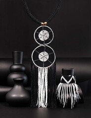 African beaded statement earrings featuring bold geometric patterns and cascading black and white strands, styled with sculptural vases for a striking monochrome fashion still life. © Valerie