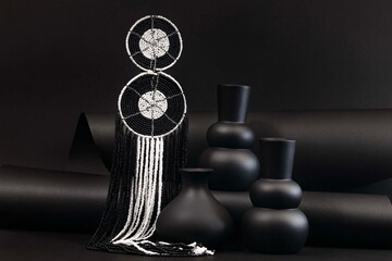 African beaded statement earrings featuring bold geometric patterns and cascading black and white strands, styled with sculptural vases for a striking monochrome fashion still life. © Valerie