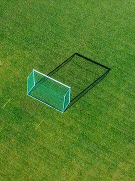 Aerial view of a soccer goal on a green grass field with a long shadow cast on the turf in Latvia.