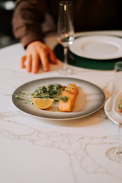 Salmon fillet served with fresh herbs and a lemon slice on a patterned plate during dinner service