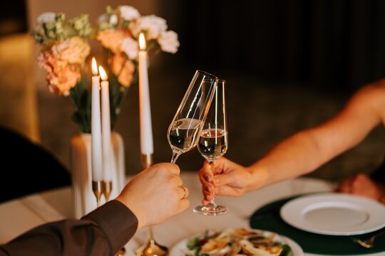 People clinking champagne glasses during a romantic candlelit dinner at a table in the evening