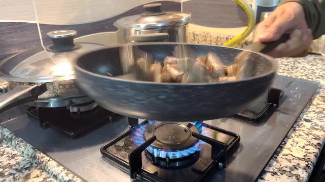 A close-up video of someone preparing food in the kitchen, cooking delicious meatballs in a Teflon skillet on the stove by shaking and turning them.