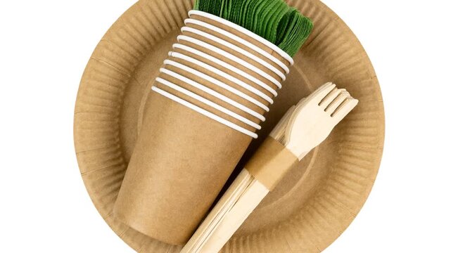 Brown kraft paper plate and cup paired with biodegradable wooden cutlery wrapped in a paper sleeve, accompanied by a green napkin, showcasing sustainable dining options for environmentally conscious.