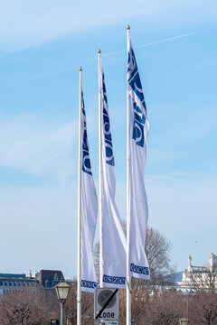 Three OSCE Flags Flying Above Cityscape Under Clear Blue Sky