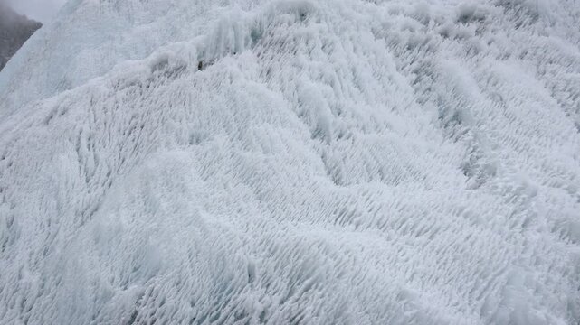 Close up detail of intricate textured surface of massive glacier, showing beautiful patterns and crevasses of dense ancient ice slowly flowing down mountainside. Climate change, melting glaciers