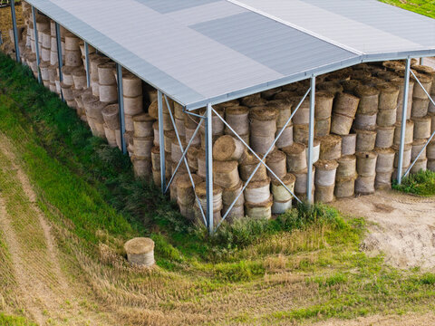 Aerial view of a large agricultural shed filled with numerous round hay bales, situated in a rural field in Virpe, Ventspils novads, Latvia.