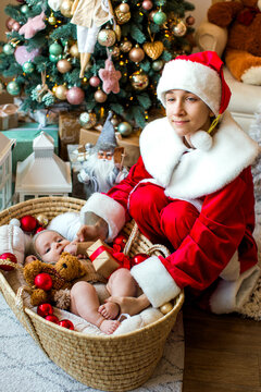 Cute baby and his teenage brother dressed as Santa Claus celebrating Christmas together at home in a cozy festive atmosphere.