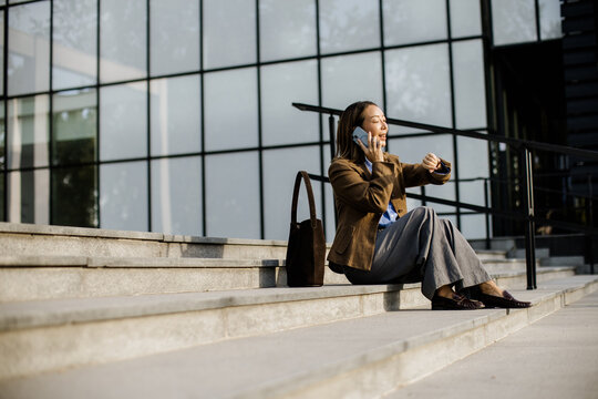 Woman sits on steps talking on phone and checking watch