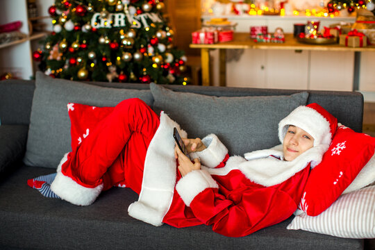 Teenage boy dressed as Santa&rsquo;s helper posing near a decorated Christmas tree at home, creating a cheerful and festive holiday atmosphere.