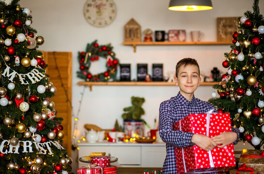 Teenage boy holding a Christmas gift near a decorated Christmas tree at home, enjoying a cozy and festive holiday atmosphere.