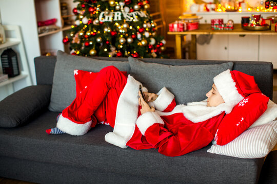 Teenage boy dressed as Santa&rsquo;s helper posing near a decorated Christmas tree at home, creating a cheerful and festive holiday atmosphere.