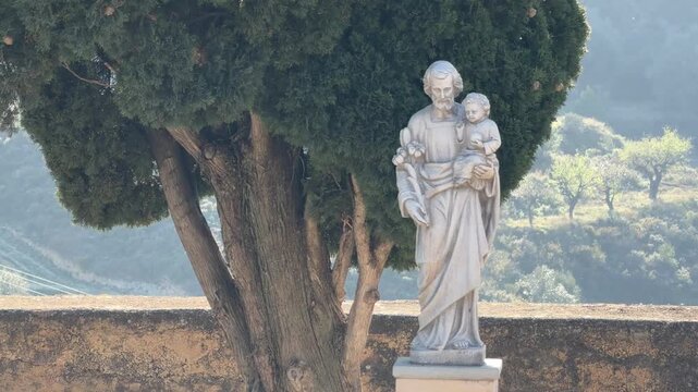 Medium angle static shot of the historic stone statue of Saint Joseph holding the Child Jesus under soft daylight in Montanejos, Castellon, Spain.