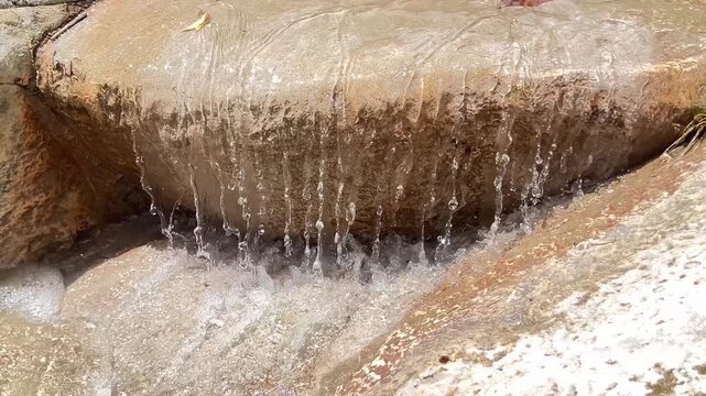 A small stone ledge releases thin streams of clear water into a shallow pool with sparkling droplets and soft white foam. High quality 4k footage