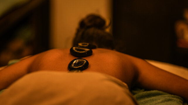 A serene woman receiving a relaxing hot stone massage treatment in a dimly lit wellness spa room