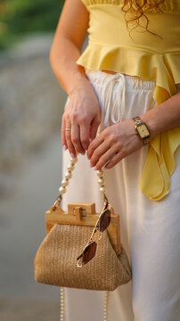 Woman holding a stylish straw handbag with pearl handle and sunglasses in summer outfit