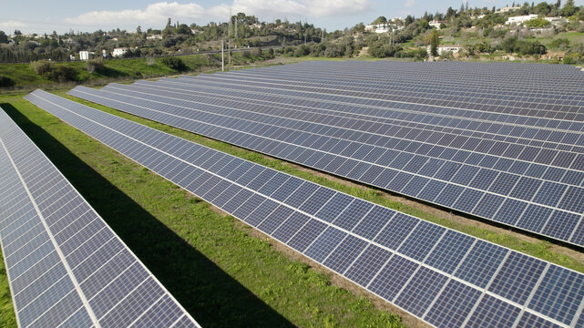 Aerial view of a large solar farm with rows of photovoltaic panels arranged in a field with green grass and rolling hills in the background in Lagos, Faro District, Portugal.