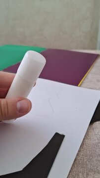 Closing a white glue stick with a cap over a crafting table in a vertical close-up shot. Vertical stock footage for stationery reviews, paper crafts, and school art preparations.