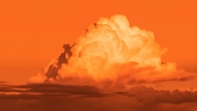 Towering clouds glow orange in sunset sky above darker layered cloud banks