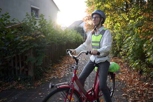 Helmeted cyclist pauses on a red city bicycle in a leafy residential lane on an autumn afternoon