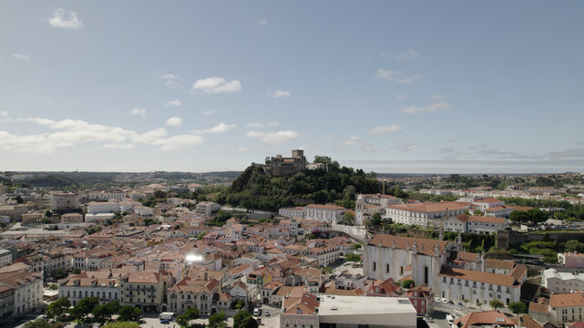 Aerial view of Leiria Castle perched on a hill overlooking the historic city center with terracotta rooftops, white buildings, and lush greenery in Leiria, Leiria District, Portugal.