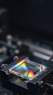 Optical glass diffraction grating mounted in laboratory instrument. Rainbow spectrum and light dispersion through precision optics. Photonics research and optical engineering.