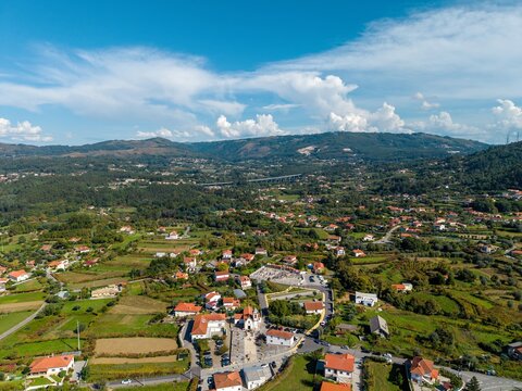 Aerial view of the church surrounded by rural houses, green fields, and the A3 highway in the distance under a blue sky in Rebordoes Santa Maria, Viana do Castelo, Portugal.