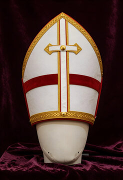 Mitre hat of a bishop, traditional catholic religious vestment with gold embroidery and red velvet trim on a display stand for church ceremony