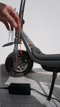 Person Plugging Power Cable into Electric Scooter Port Outdoors