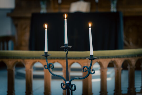 Three Burning White Candles on Wrought Iron Candelabrum Inside a Church
