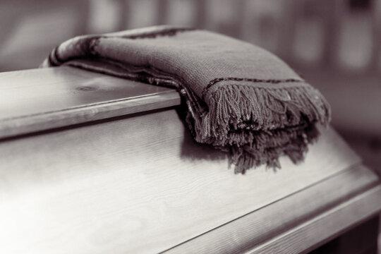 Folded Funeral Blanket with Fringes Resting on a Wooden Coffin Lid