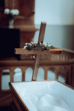 Wooden Cross with Floral Decoration Beside an Open White Lined Coffin in Church