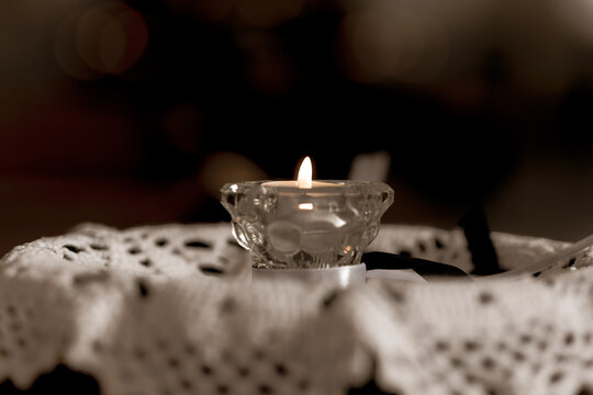 Burning Memorial Candle in Glass Holder on White Lace Cloth