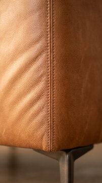 Tactile cognac leather upholstery detail with stitched seam and metal leg, soft focus background